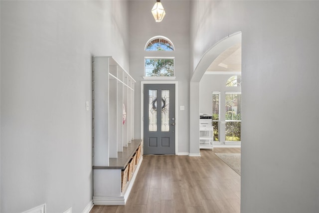 entryway with baseboards, arched walkways, wood finished floors, and a towering ceiling