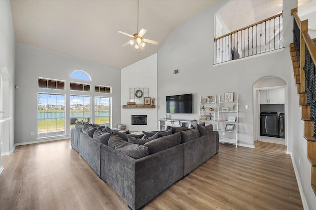 living area featuring wood finished floors, a ceiling fan, washing machine and clothes dryer, arched walkways, and a large fireplace