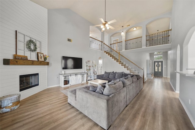 living area with visible vents, wood finished floors, a large fireplace, arched walkways, and baseboards