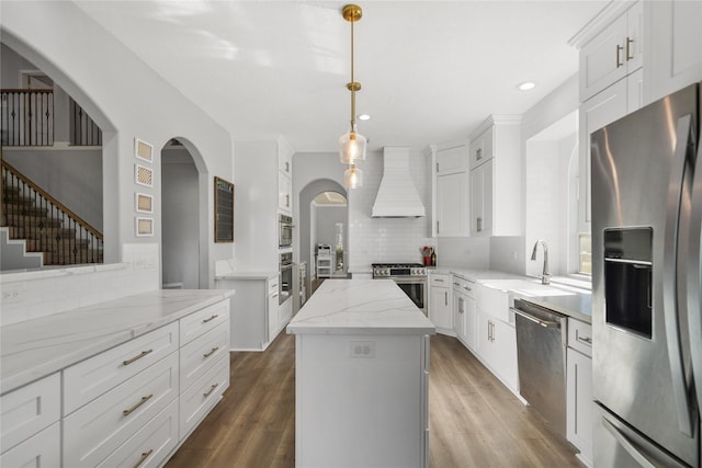 kitchen with custom range hood, wood finished floors, a center island, stainless steel appliances, and white cabinets