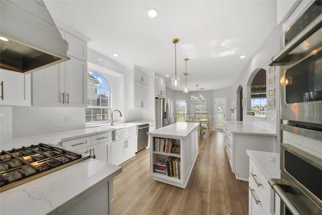 kitchen with tasteful backsplash, light wood finished floors, a kitchen island, range hood, and stainless steel appliances