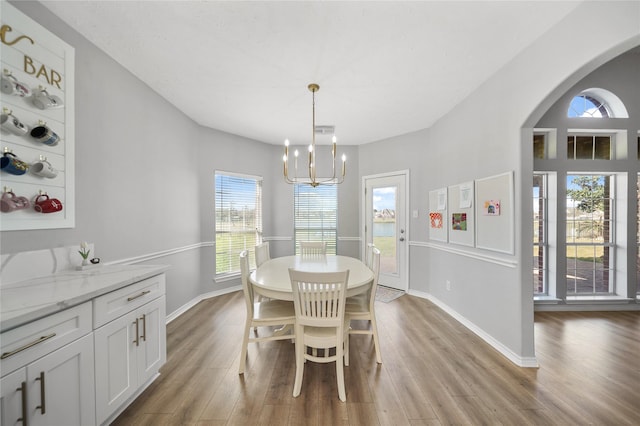 dining space with visible vents, baseboards, light wood-style flooring, arched walkways, and a notable chandelier