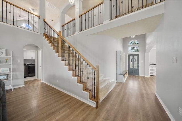 foyer with washer and clothes dryer, wood finished floors, stairway, arched walkways, and a towering ceiling