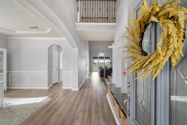 entrance foyer featuring visible vents, a tray ceiling, wood finished floors, arched walkways, and a decorative wall