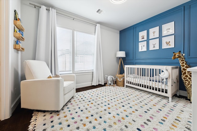 bedroom with a decorative wall, a nursery area, baseboards, and visible vents