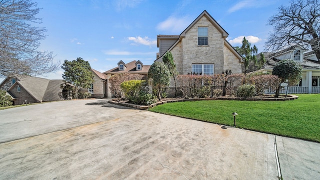 view of front facade featuring stone siding, concrete driveway, a front lawn, and fence