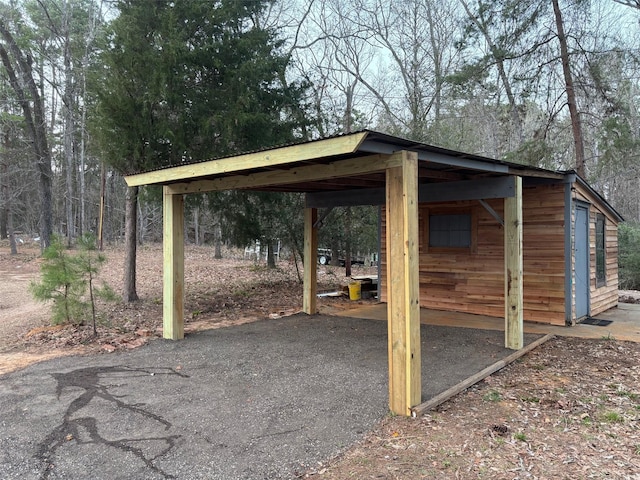 view of outbuilding featuring aphalt driveway, a carport, and an outdoor structure