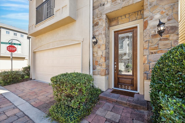 entrance to property with stone siding, stucco siding, and decorative driveway