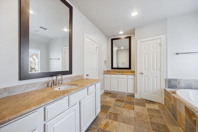 full bath featuring stone tile flooring, visible vents, two vanities, and a sink