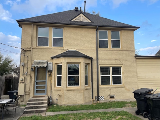 rear view of property featuring entry steps, cooling unit, brick siding, and roof with shingles