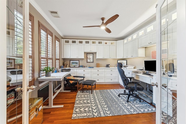 office space with visible vents, wood finished floors, built in desk, and ornamental molding