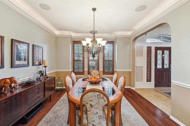 dining space with a chandelier, arched walkways, wood finished floors, and crown molding