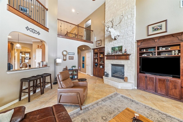 living area with visible vents, tile patterned floors, baseboards, a stone fireplace, and arched walkways