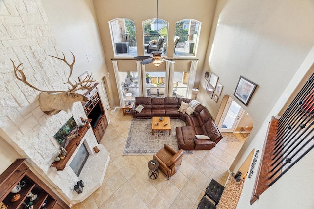 tiled living area featuring arched walkways, a glass covered fireplace, a ceiling fan, and a towering ceiling