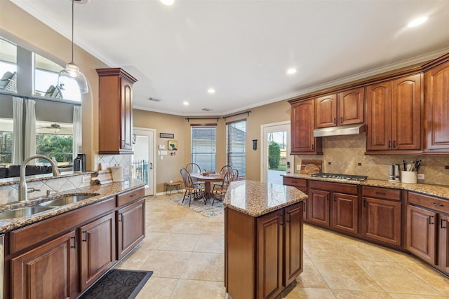 kitchen with a sink, under cabinet range hood, a kitchen island, crown molding, and stainless steel gas cooktop