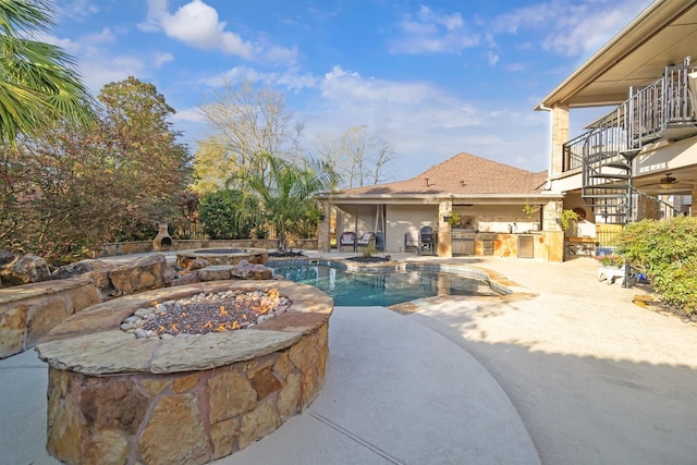 pool with a patio area, an outdoor kitchen, a fire pit, and stairs