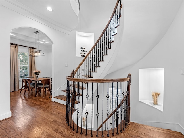 staircase with a notable chandelier, wood finished floors, recessed lighting, arched walkways, and crown molding