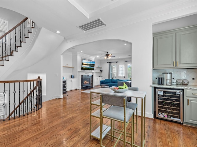 interior space featuring visible vents, wine cooler, a tiled fireplace, wood finished floors, and arched walkways