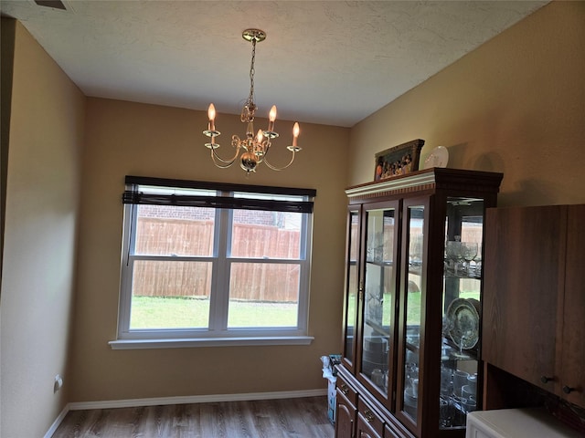 dining space featuring baseboards, a notable chandelier, wood finished floors, and a textured ceiling