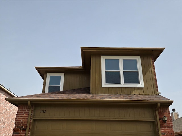 view of front facade featuring a garage, brick siding, and roof with shingles