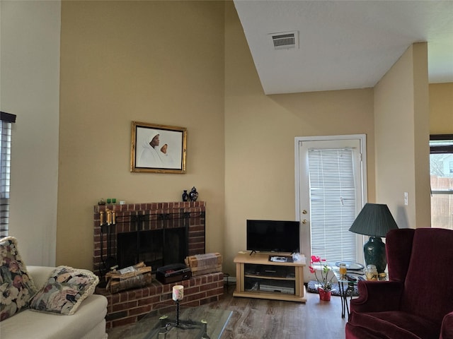 living area featuring a brick fireplace, wood finished floors, and visible vents