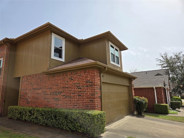 view of side of property with a garage, brick siding, driveway, and a shingled roof