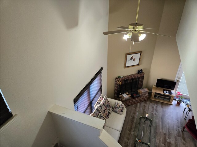 living area featuring a ceiling fan, wood finished floors, a high ceiling, and a fireplace