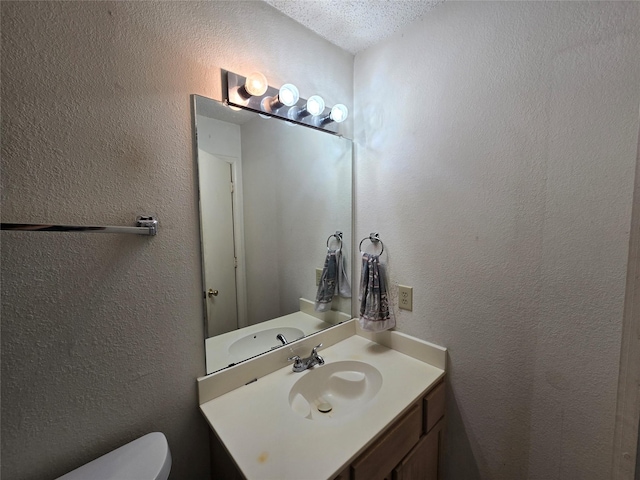 half bathroom with toilet, vanity, and a textured wall