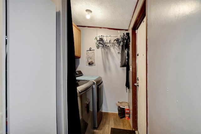 washroom with light wood finished floors, cabinet space, washer and dryer, and a textured ceiling