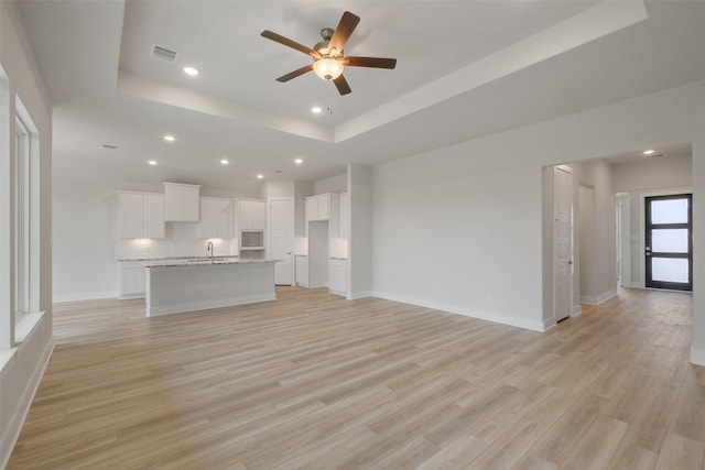 unfurnished living room with light wood finished floors, visible vents, baseboards, a tray ceiling, and a sink