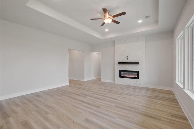 unfurnished living room featuring a raised ceiling, a fireplace, and light wood-style floors