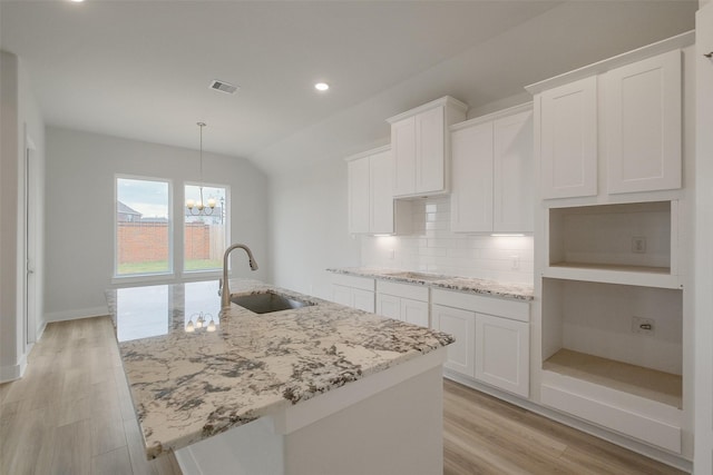 kitchen with a sink, light wood-type flooring, an island with sink, and decorative backsplash