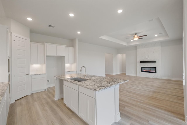 kitchen with light wood finished floors, a large fireplace, a tray ceiling, white cabinetry, and a sink