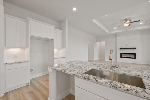 kitchen with a sink, light stone countertops, a raised ceiling, and white cabinetry