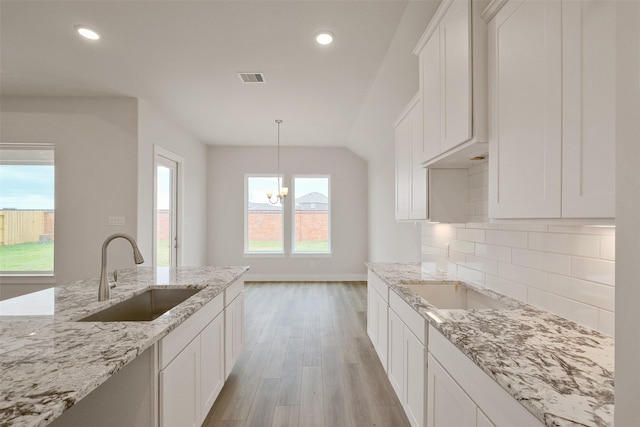 kitchen with a sink, white cabinetry, light wood finished floors, decorative backsplash, and light stone countertops