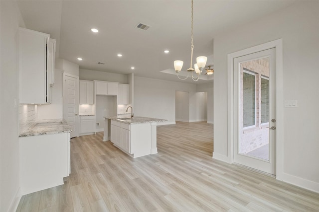 kitchen with white cabinetry, light wood-style flooring, light stone counters, and visible vents