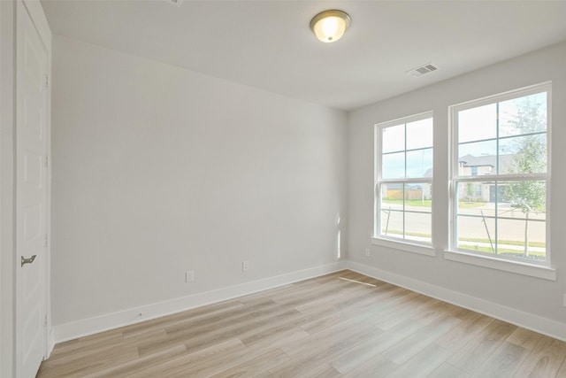 empty room featuring plenty of natural light, light wood-style flooring, baseboards, and visible vents