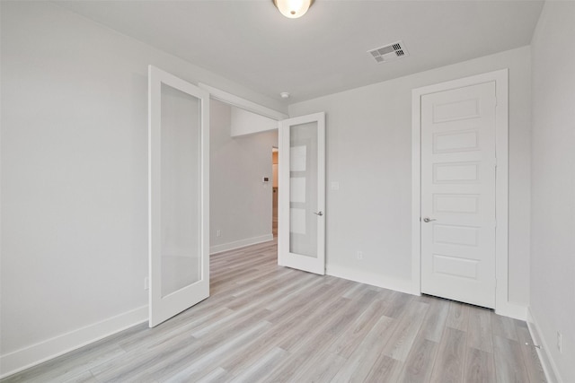 spare room with light wood-type flooring, visible vents, and baseboards