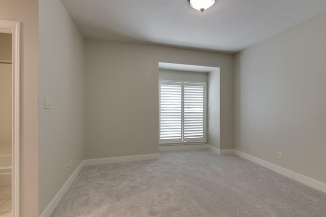 spare room featuring light colored carpet and baseboards