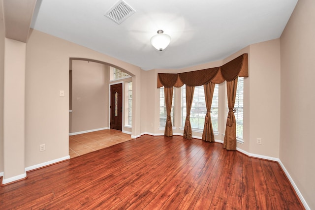 spare room featuring visible vents, wood-type flooring, arched walkways, and baseboards