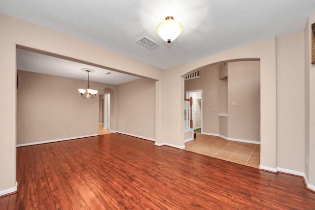 unfurnished room with visible vents, arched walkways, wood finished floors, and a chandelier