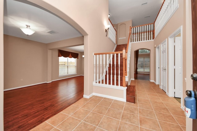 entryway featuring arched walkways, light tile patterned floors, stairway, and baseboards