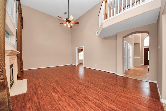 unfurnished living room with wood finished floors, baseboards, arched walkways, ceiling fan, and a glass covered fireplace