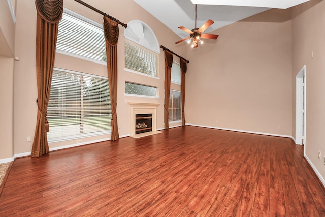 unfurnished living room with a fireplace, a high ceiling, ceiling fan, and wood finished floors