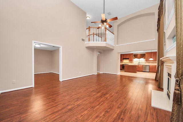 unfurnished living room with baseboards, visible vents, ceiling fan, hardwood / wood-style flooring, and a glass covered fireplace