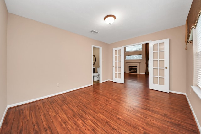 empty room featuring a fireplace, wood finished floors, french doors, and baseboards