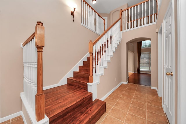 staircase with tile patterned flooring, arched walkways, a high ceiling, and baseboards