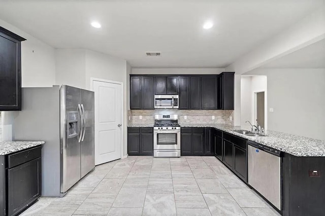 kitchen featuring visible vents, a peninsula, a sink, stainless steel appliances, and backsplash