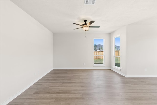 unfurnished room featuring baseboards, wood finished floors, visible vents, and ceiling fan