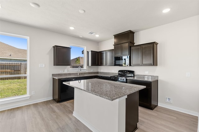 kitchen featuring light stone countertops, visible vents, a sink, black appliances, and light wood-style floors